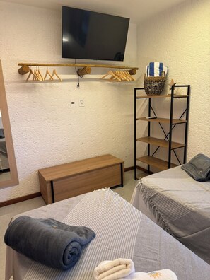 A hotel room with a bed, a bench, a TV mounted on the wall, and a shelf with a basket.