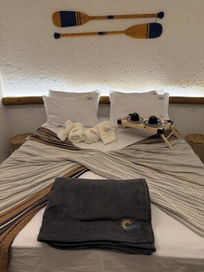 Una cama bien hecha con una toalla doblada, una bandeja con una tetera y tazas, y dos palas de madera en la pared.