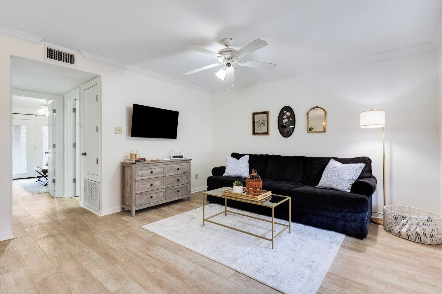 Un salon avec un canapé noir, un meuble en bois, une table basse et un ventilateur de plafond.