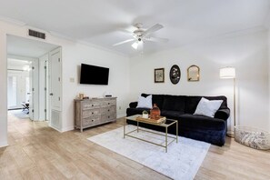 Ein Wohnzimmer mit einem schwarzen Sofa, einem Holzschrank, einem Couchtisch und einem Deckenventilator.