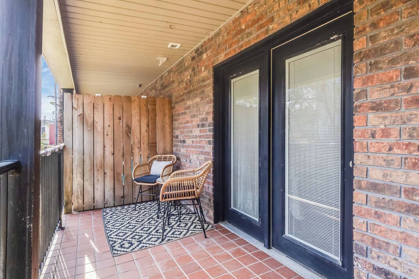 Un patio couvert avec un mur en briques, deux portes-fenêtres coulissantes et une petite table avec des chaises.