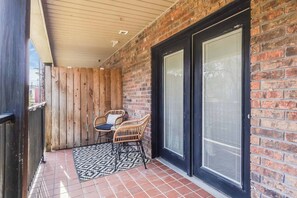 Ein überdachter Patio-Bereich mit Backsteinmauer, zwei Terrassentüren und einem kleinen Tisch mit Stühlen.