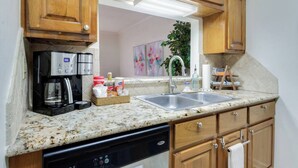 A kitchen with wooden cabinets, a coffee maker, a sink, and a dishwashing unit. - Cozy 1BR Condo w/Balcony - Near UL & Ochsner - Apartment (Lafayette)