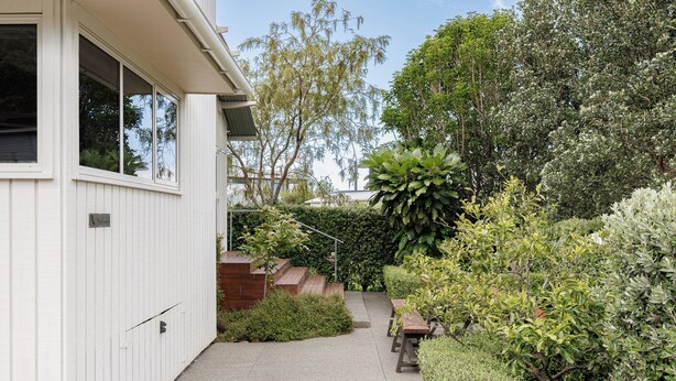 A residential property with a paved driveway, a wooden deck, and various shrubs and trees.