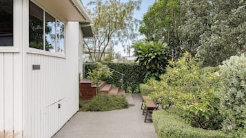 A residential property with a paved driveway, a wooden deck, and various shrubs and trees.