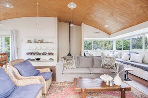 A spacious living room with a high ceiling, a sofa set, wicker chairs, a coffee table, and a fireplace.