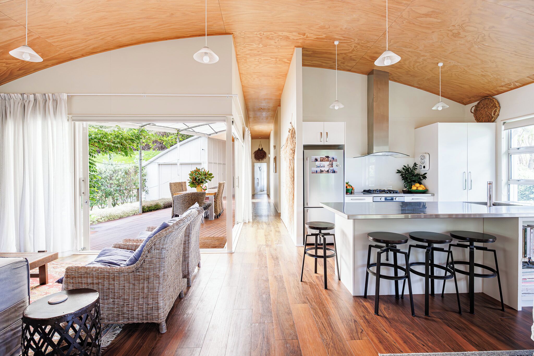 A modern kitchen with a central island, bar stools, and a dining area with a wicker sofa and table.