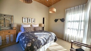 A bedroom with a bed, a dresser, a lamp, and a window with curtains.