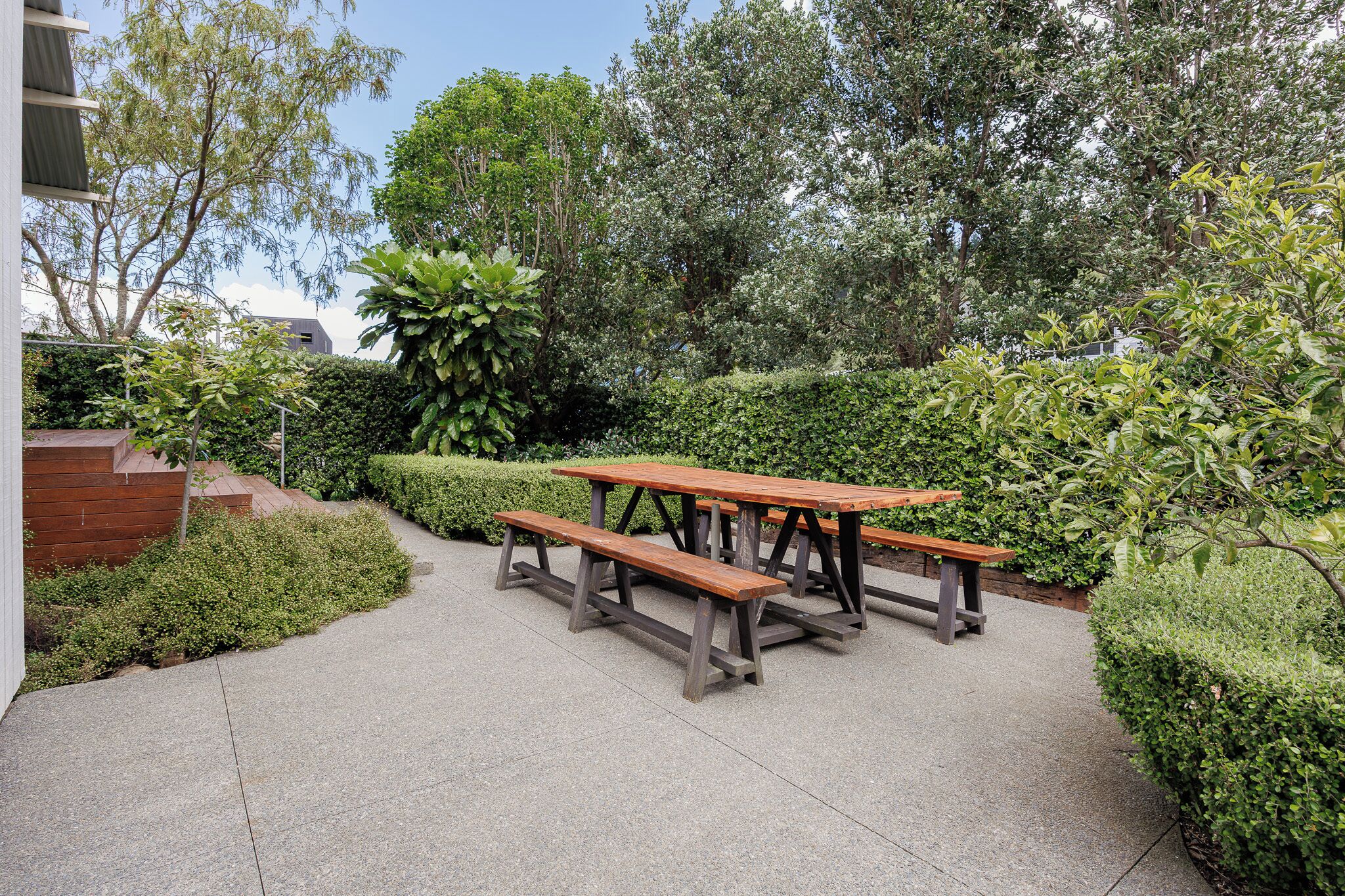 Un espacio exterior pavimentado con mesas de picnic de madera y vegetación circundante.