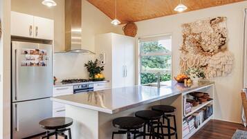 A modern kitchen with a large island, stainless steel appliances, and a view of greenery outside.