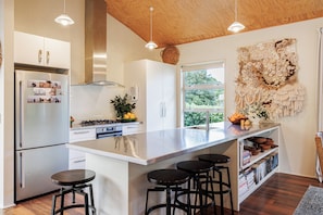 A modern kitchen with a large island, stainless steel appliances, and a view of greenery outside.
