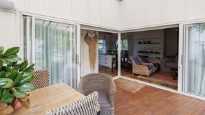 A modern interior with a dining area, a seating area with wicker furniture, and a kitchen visible through an open door.