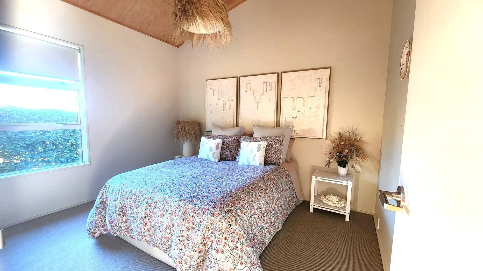 A bedroom with a bed, a nightstand, a window, and wall art.