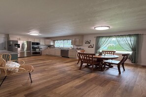 A spacious kitchen with wooden flooring, a dining area with a table and chairs, and a view of greenery outside. - Summit Place - 10 Minutes to Ft Leonard Wood - Easy In and Out - Fenced Yard (Waynesville)