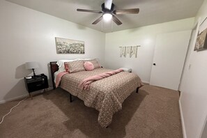 A bedroom with a bed, a nightstand, a ceiling fan, a wall-mounted artwork, and a door. - Summit Place - 10 Minutes to Ft Leonard Wood - Easy In and Out - Fenced Yard (Waynesville)