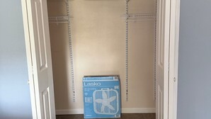 Un placard dont les portes sont ouvertes, une tringle à vêtements et une boîte étiquetée « Ventilateur Lasko ».