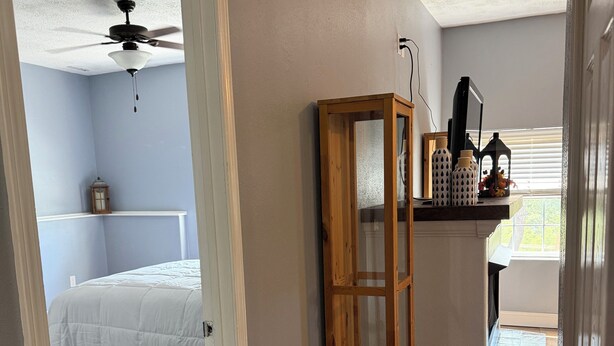 Une chambre à coucher comprenant un lit, une table de chevet, une armoire en bois et un ventilateur de plafond.