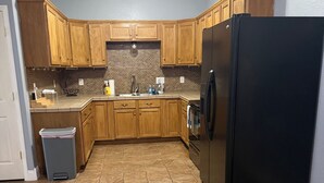 A kitchen with wooden cabinets, a black refrigerator, and a tiled floor.