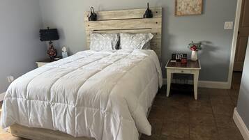A bedroom with a bed, a nightstand, a wall clock, and a small table with a vase.
