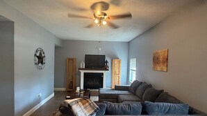 A living room with a dark gray sofa, a fireplace, a ceiling fan, and a television.