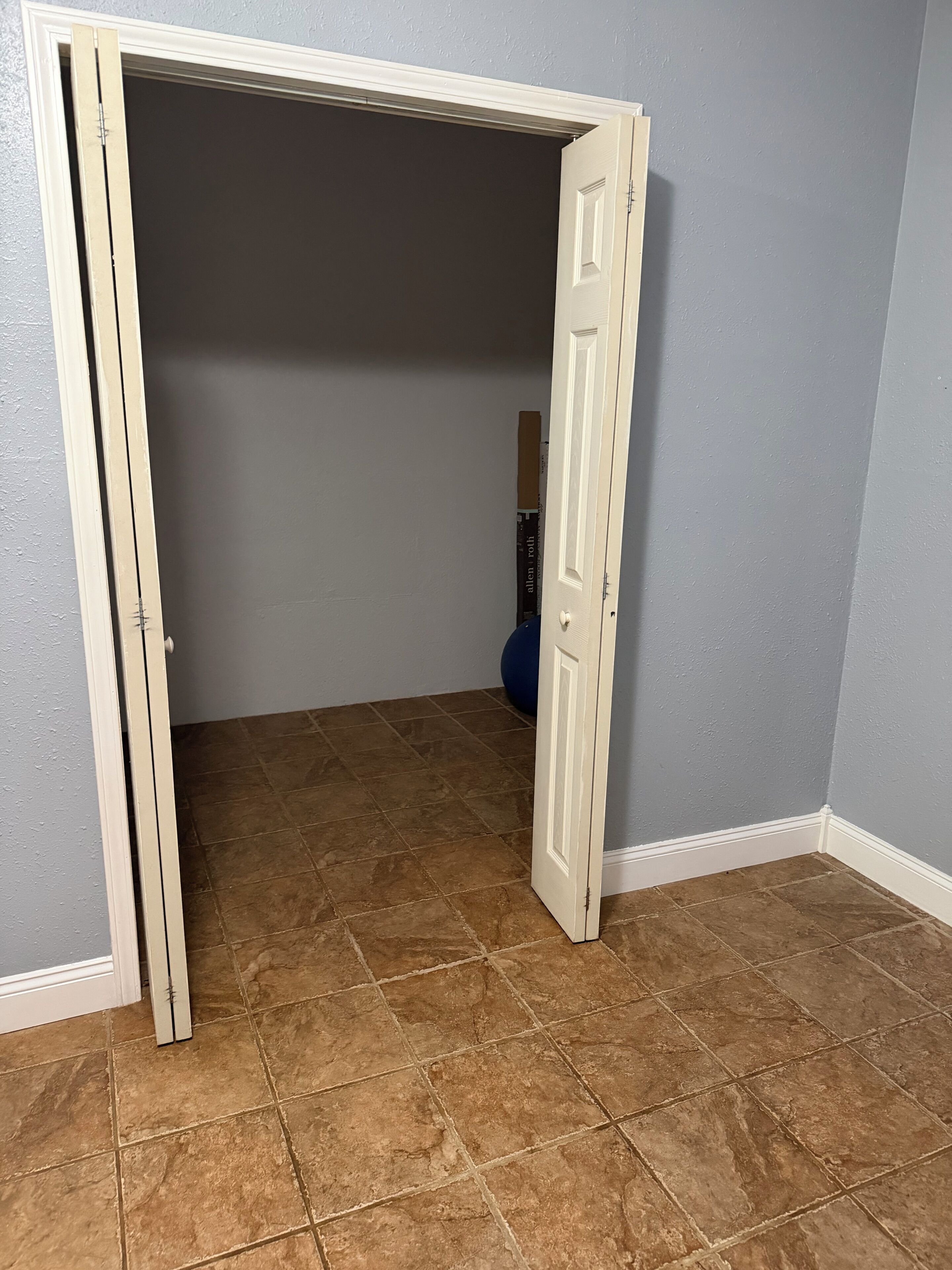 A room with a partially open door, brown tiled floor, and a blue exercise ball in the background.