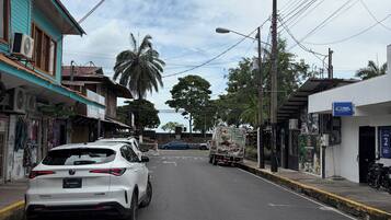 A street with a white car parked on the side, a truck in the distance, and buildings with various signs and awnings.