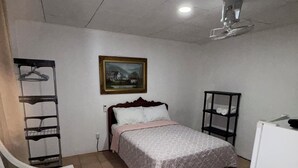 Ein Schlafzimmer mit Bett, Stuhl, Kommode, einem Bild an der Wand und einem Deckenventilator.