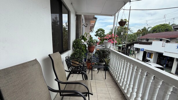 Ein Balkon mit zwei Stühlen, Blumentöpfen und einem weißen Geländer.