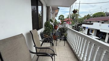 A balcony with two chairs, potted plants, and a white railing.
