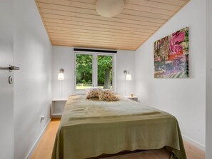A bedroom with a bed, two bedside lamps, a window with a view of greenery, and a colorful abstract painting on the wall. - "Elenora" - 200m from the sea by Interhome (Odder)