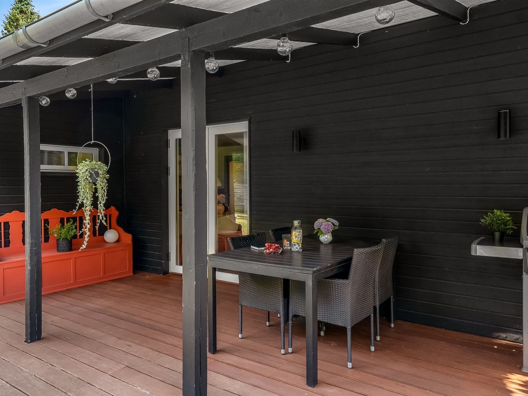 Une terrasse extérieure avec une table et des chaises, une plante suspendue et un banc rouge.