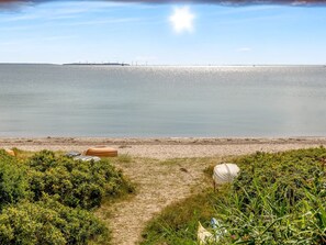 Une plage offrant une vue dégagée sur la mer, un sentier sablonneux et quelques plantes.