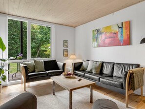 A modern living room with a black leather sofa, a wooden coffee table, and a large window with a view of greenery. - "Elenora" - 200m from the sea by Interhome (Odder)