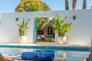 Ein Pool mit Blick auf ein Haus durch eine offene Mauer, mit Topfpflanzen und einem blauen Handtuch am Poolrand.