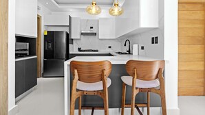 Eine moderne Küche mit einer zentralen Kochinsel, zwei Barhocker, Edelstahlgeräten und Pendelleuchten.