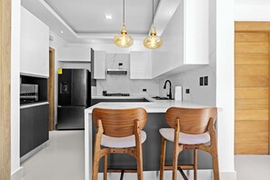 A modern kitchen with a central island, two bar stools, stainless steel appliances, and pendant lighting. - NOK Elegant 3BR Villa with Private Pool (Punta Cana)