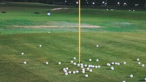 Ein Golfplatz bei Nacht mit einer Fahne auf einem Mast und verstreuten Golfbällen.