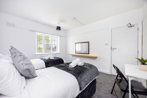 Een slaapkamer met twee bedden, een raam, een spiegel, een bureau en een stoel.