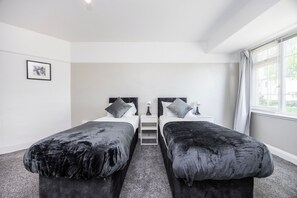 A hotel room with two beds, a window with blinds, a framed picture on the wall, and a carpeted floor. - 8 Bed - Sleeps 14 - Large Garden - Parking 10 Cars (Tilbury)