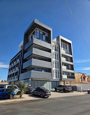 A multi-story building with balconies and large windows, located in an urban setting with parked cars. - Cozy Loft with Panoramic View in Chihuahua (Chihuahua)