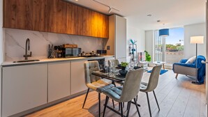 A modern kitchen with a built-in coffee bar, dining area with chairs and a table, and a living room with a sofa and a TV. - Stylish Central Birmingham 1Bed Apartment (Birmingham)