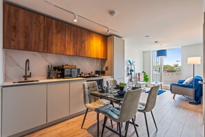 A modern kitchen with a built-in coffee bar, dining area with chairs and a table, and a living room with a sofa and a TV. - Stylish Central Birmingham 1Bed Apartment (Birmingham)