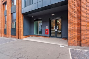 A modern building entrance with a brick facade, large glass doors, and a fire safety exit sign. - Stylish Central Birmingham 1Bed Apartment (Birmingham)