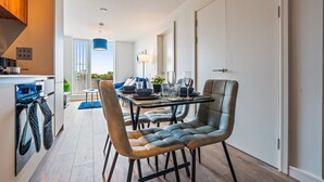 A modern kitchen with a dining area, featuring a large window, a blue pendant light, and a dining table set for four. - Stylish Central Birmingham 1Bed Apartment (Birmingham)