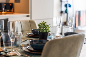 Una mesa de comedor dispuesta con platos, vasos y cubiertos, con una planta en maceta en el centro.