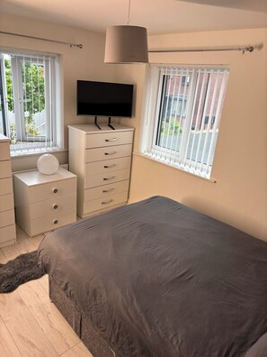 Ein Schlafzimmer mit einem Bett, einem Schminktisch, einem Fernseher und einem Fenster mit Jalousien.