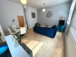 Ein modernes Wohnzimmer mit einer Couch, einem Esstisch mit Stühlen, einer Wanduhr und einem Fenster mit Jalousien.