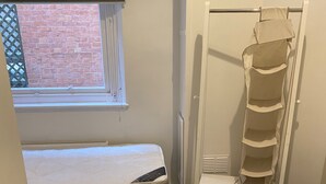 Um quarto com uma cama, uma janela com persianas, um radiador e um móvel para guardar objetos.
