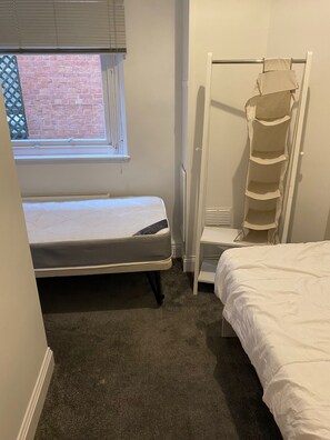Ein Schlafzimmer mit Bett, einem Fenster mit Jalousien, einem Heizkörper und einem Stauraum.