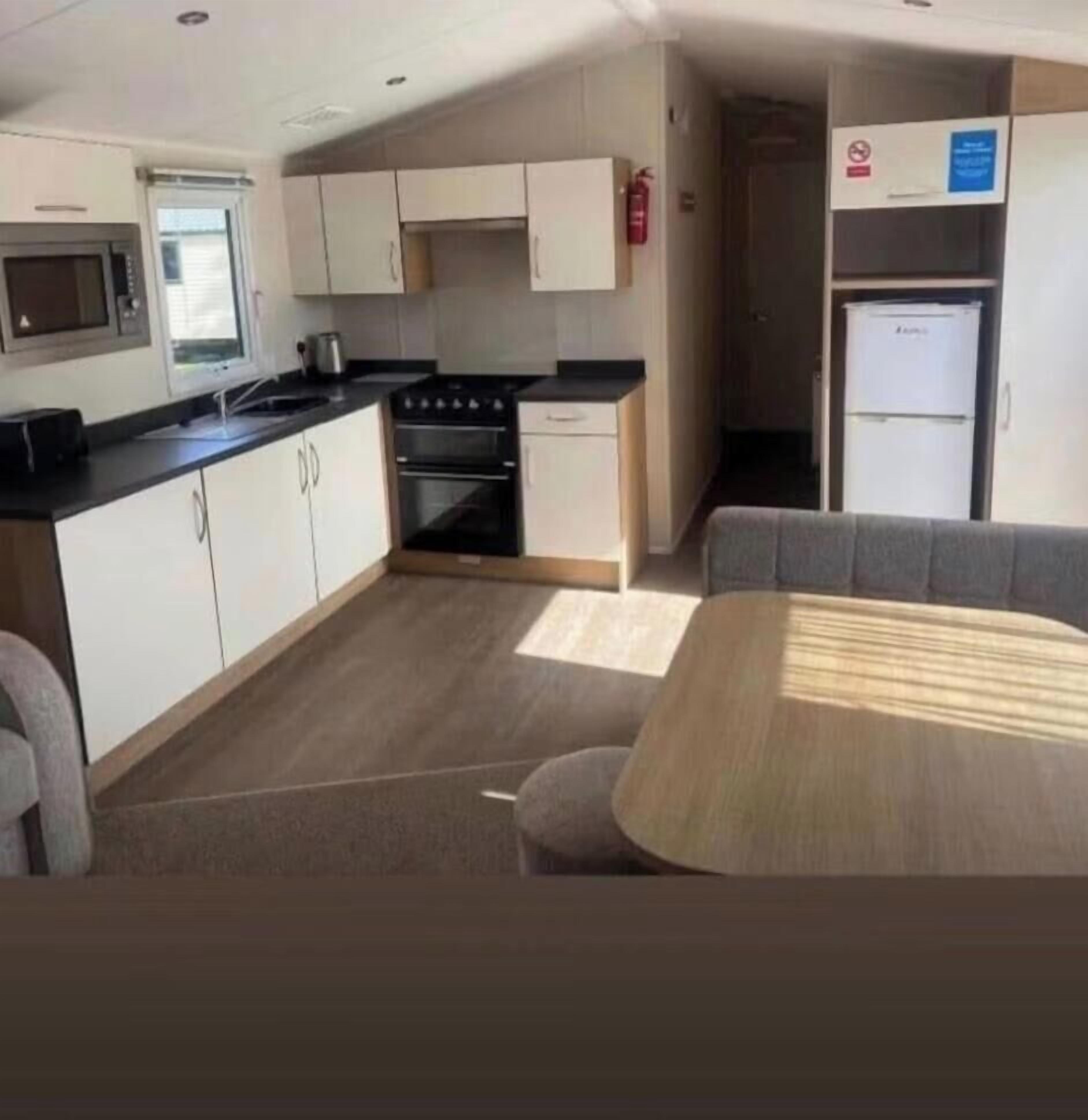 A compact kitchenette with a microwave, stove, and sink, a small dining area with a table and chairs, and a refrigerator.
